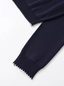 Detail of navy blue knit polo shirt with white scalloped contrast stitching on sleeve hem