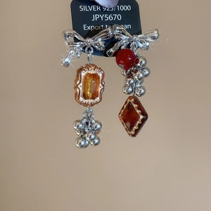 Close-up of asymmetric bow earrings featuring red beads and amber resin charms