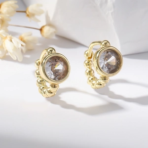 Gold beaded hoop earrings with grey round cut zircon crystals on a minimalist white background