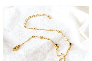 Detail of gold titanium anklet with black white round beads and white star pendant charms