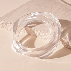 Detailed close-up of a clear twisted resin acrylic bangle on a textured stone surface