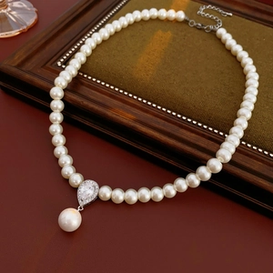 Detail of elegant pearl necklace featuring a zircon water drop pendant on vintage wood