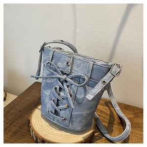 Détail du sac seau en denim bleu clair avec laçage style corset et boucle en métal argent