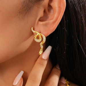 Close-up of gold snake earrings featuring shimmering pavé crystals and red rhinestone eyes