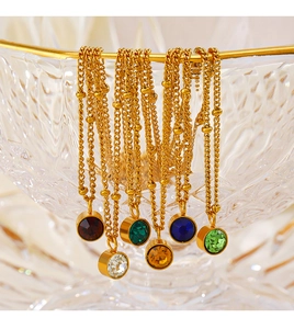 Detail of 18K gold stainless steel birthstone necklaces draped over a crystal bowl