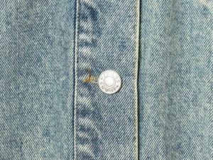 Close-up of light blue denim fabric texture and silver metal button with JEANS engraving
