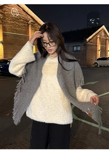 Detail of grey fringe knitted scarf and white fuzzy sweater in a cozy outdoor night setting