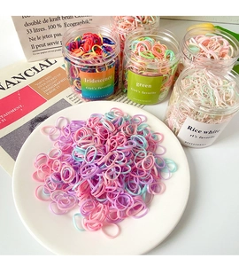 Colorful elastic hair ties in transparent jars and scattered on a white tray detail