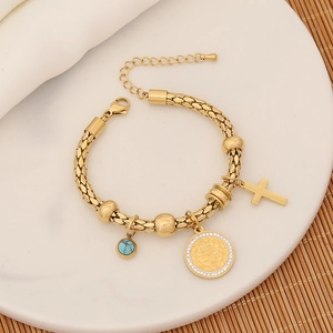 Detail of gold woven bracelet with cross, saint medal and turquoise pendants on white plate