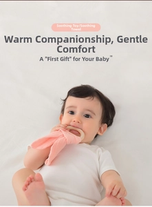Baby chewing on pink cotton gauze comforter towel with natural wooden teething ring toy