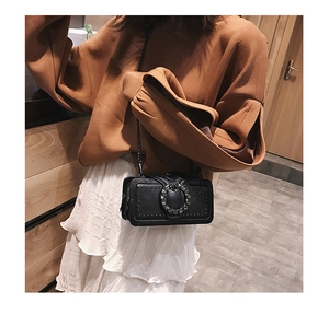 Detail of black leather crossbody bag featuring a crystal-studded buckle and metal chain