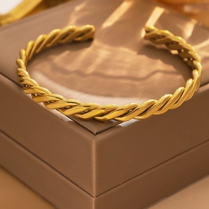 Detailed view of an 18k gold-plated stainless steel twisted rope cuff on a jewelry box