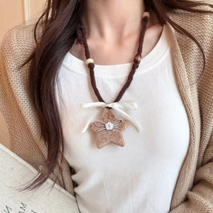 Detail of plush star necklace featuring brown star pendant and cream ribbon on woven rope