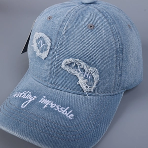 Dettaglio cappello baseball in denim con ricamo Nothing Impossible e strappi decorativi
