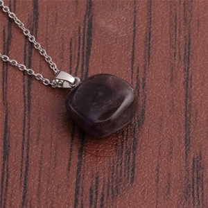 Close-up of deep purple natural stone pendant necklace with silver chain on wood surface