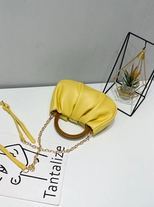 Detail of yellow pleated cloud bag featuring a circular wooden handle and gold chain strap