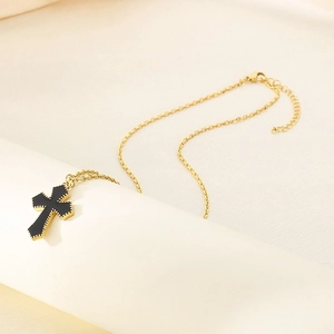 Detail of gold cross necklace with black enamel inlay and textured beaded edges