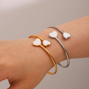Detail of 18k gold stainless steel open bangle with white enamel heart charm on wrist