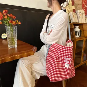 Detail of red and white plaid tote bag featuring a pink woven label and blue strap