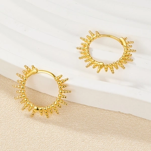 Detailed close-up of golden sunburst hoop earrings on elegant textured fabric background