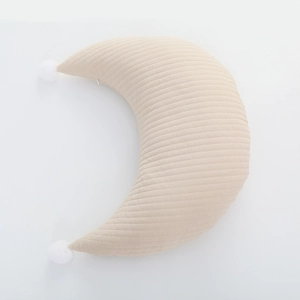 Detail of moon-shaped cotton breastfeeding pillow with quilted texture and pom-pom trim