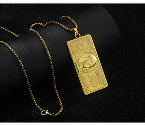 Close-up of gold 100 dollar bill pendant necklace with detailed engraved relief on black surface