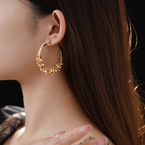 Grosse créole dorée avec breloques fleurs portée par un mannequin en vue de profil chic