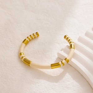 Close-up of gold and cream enamel striped bangle on a minimalist textured fabric background