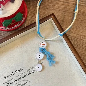 Vue détaillée du pendentif bonhomme de neige avec écharpe bleue sur décor festif