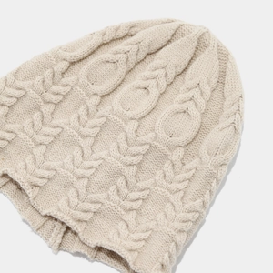 Close-up of beige cable knit beanie showing thick wool texture and warm braided pattern