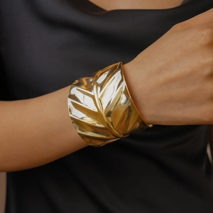 Macro view of wide gold leaf cuff bracelet featuring detailed vein texture and mirror finish