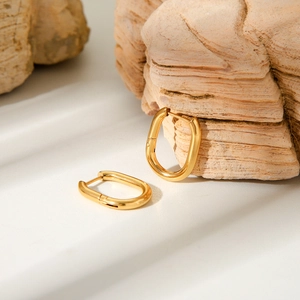 Macro detail of polished 18K gold plated oval hoop earrings on a textured stone