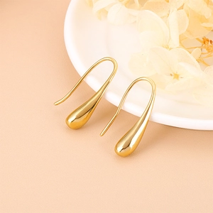 Close-up of golden teardrop earrings on a white plate with elegant dried flower decor