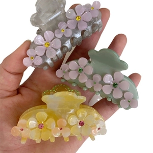 Three acetate flower hair claws in gray, green, and yellow with rhinestone accents