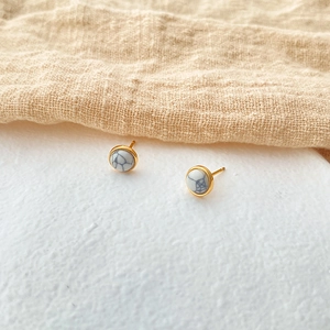 Detail of round white natural stone earrings with gold plating on textured fabric