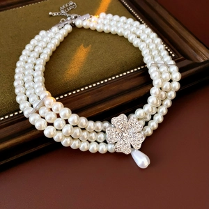 Detailed macro of a triple-layer pearl necklace with a crystal clover pendant and drop charm