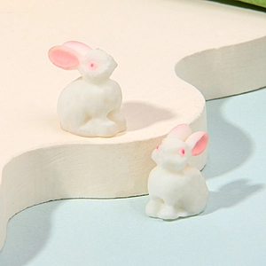 Close-up of two miniature white resin rabbits on a cream wavy stand with light blue backdrop