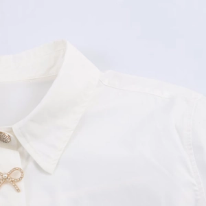 Detail of white poplin shirt featuring gold bow pearl buttons and rhinestone accents