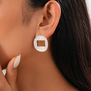 Close-up of silver oval stud earrings with brown rectangular inlay on a model