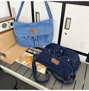 Détail de sacs bandoulière en denim bleu clair et foncé avec écusson cuir sur banc en bois