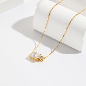 Macro shot of gold necklace featuring rectangular and round clear crystals on white pedestal