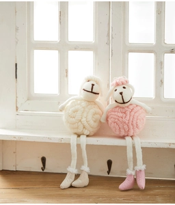 Close-up of handmade wool felt sheep dolls in cream and pink on a white windowsill
