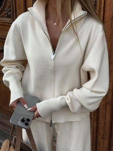 Detail of soft white knitted zip-up hoodie with ribbed cuffs and natural wood background