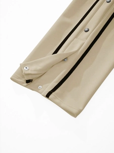 Close-up of beige joggers featuring side snap buttons and black athletic side stripes