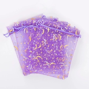 Stack of purple organza gift bags with gold foil stars and moon patterns on white background