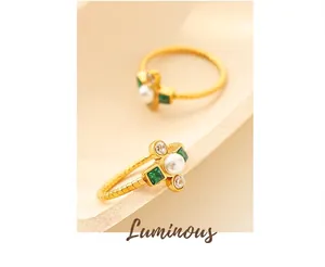 Macro detail of gold ring with central pearl, emerald gems and twisted band