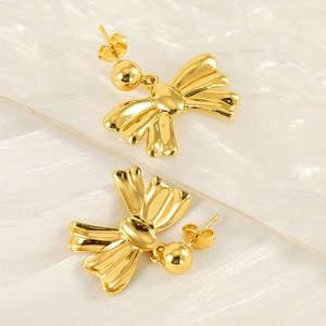Elegant gold bow earrings with polished beads on silk and ice texture background