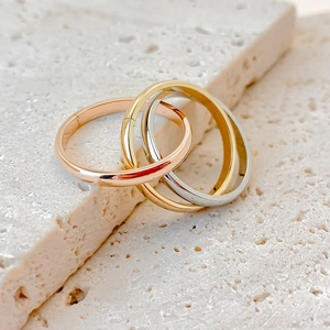 Minimalist tricolor interlocking stainless steel rings on a textured stone background