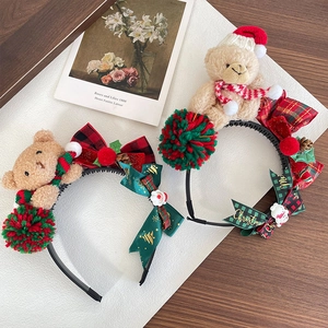 Christmas bear headband with red green pom poms and festive bow on a textured tray