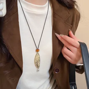 Close-up of leather leaf pendant necklace with amber bead on a brown blazer outfit